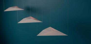 Three paper airplanes suspended by threads against a cerulean blue background.