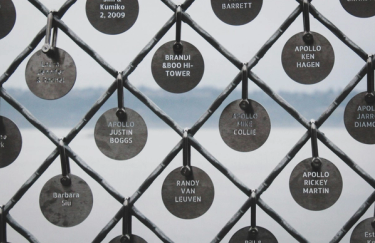 Diamond patterned wire fence with small circular metal tags printed with names hanging from each vertice