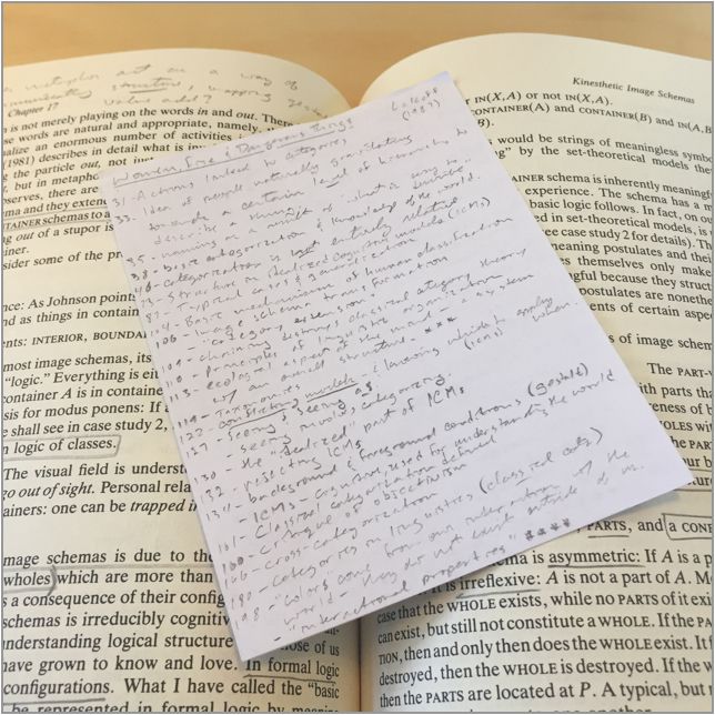 An open book with a small sheet of hand-written notes sitting on top of it
