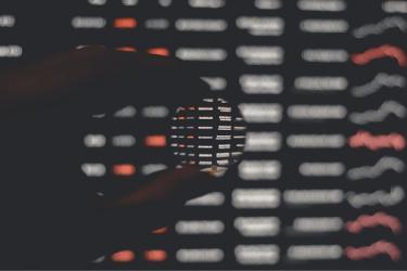 A hand holding a clear spherical lens up to a computer screen of data