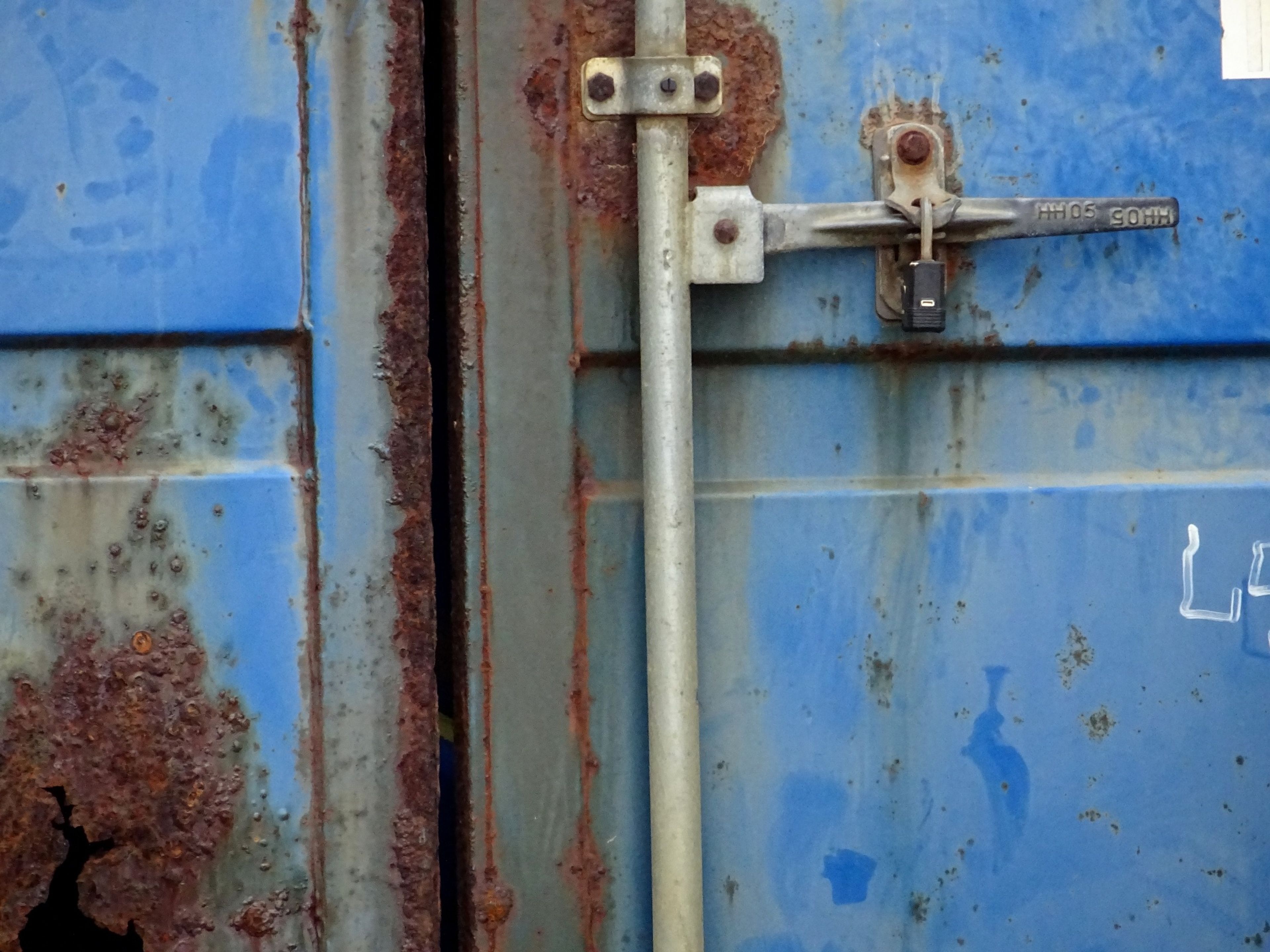 Rusted blue container door with a locking bar, handle, and padlock