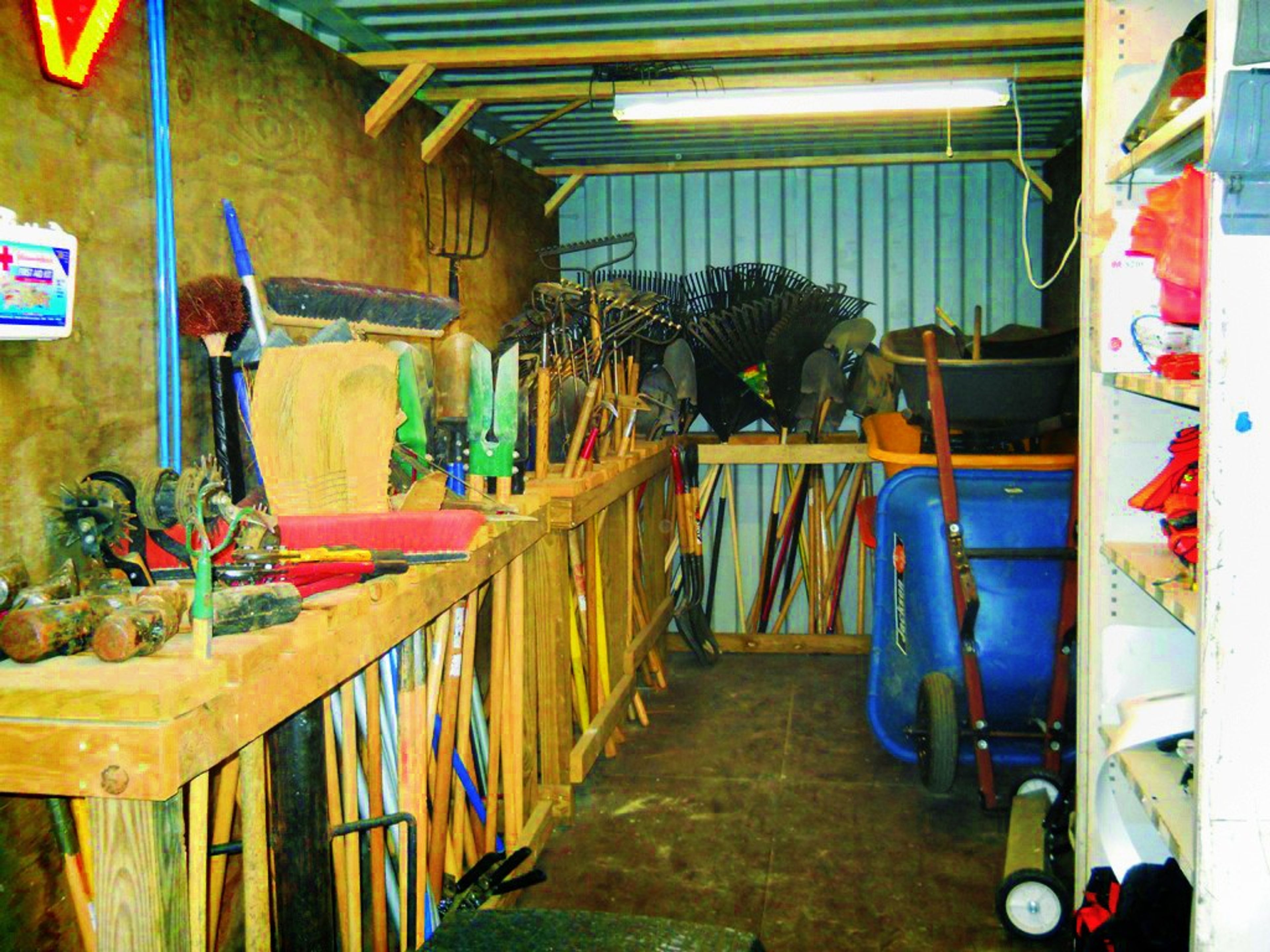 Rakes, shovels, and supplies organized along racks and shelves inside a storage container