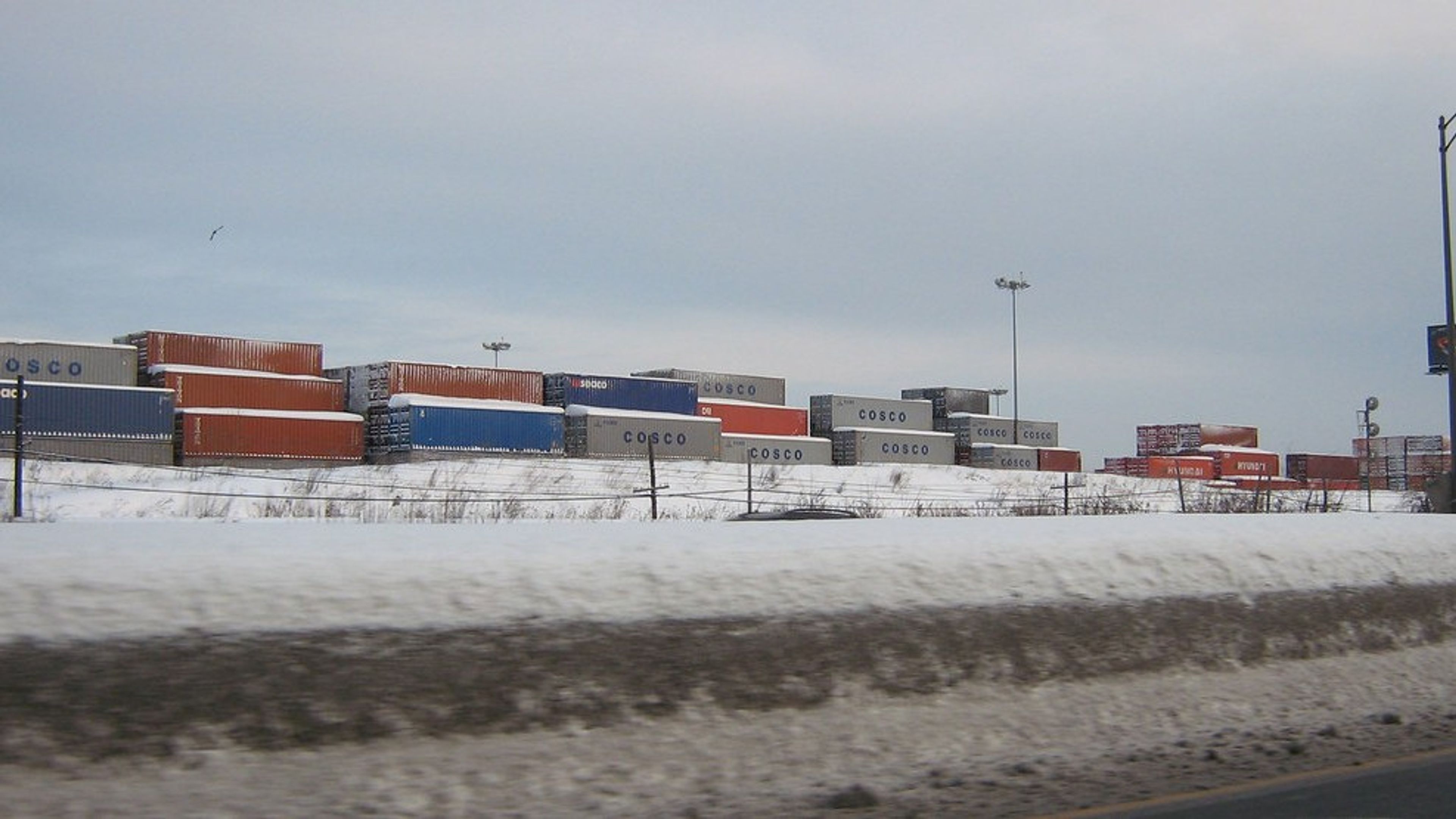 Stacked shipping containers in a snow-covered container yard in winter