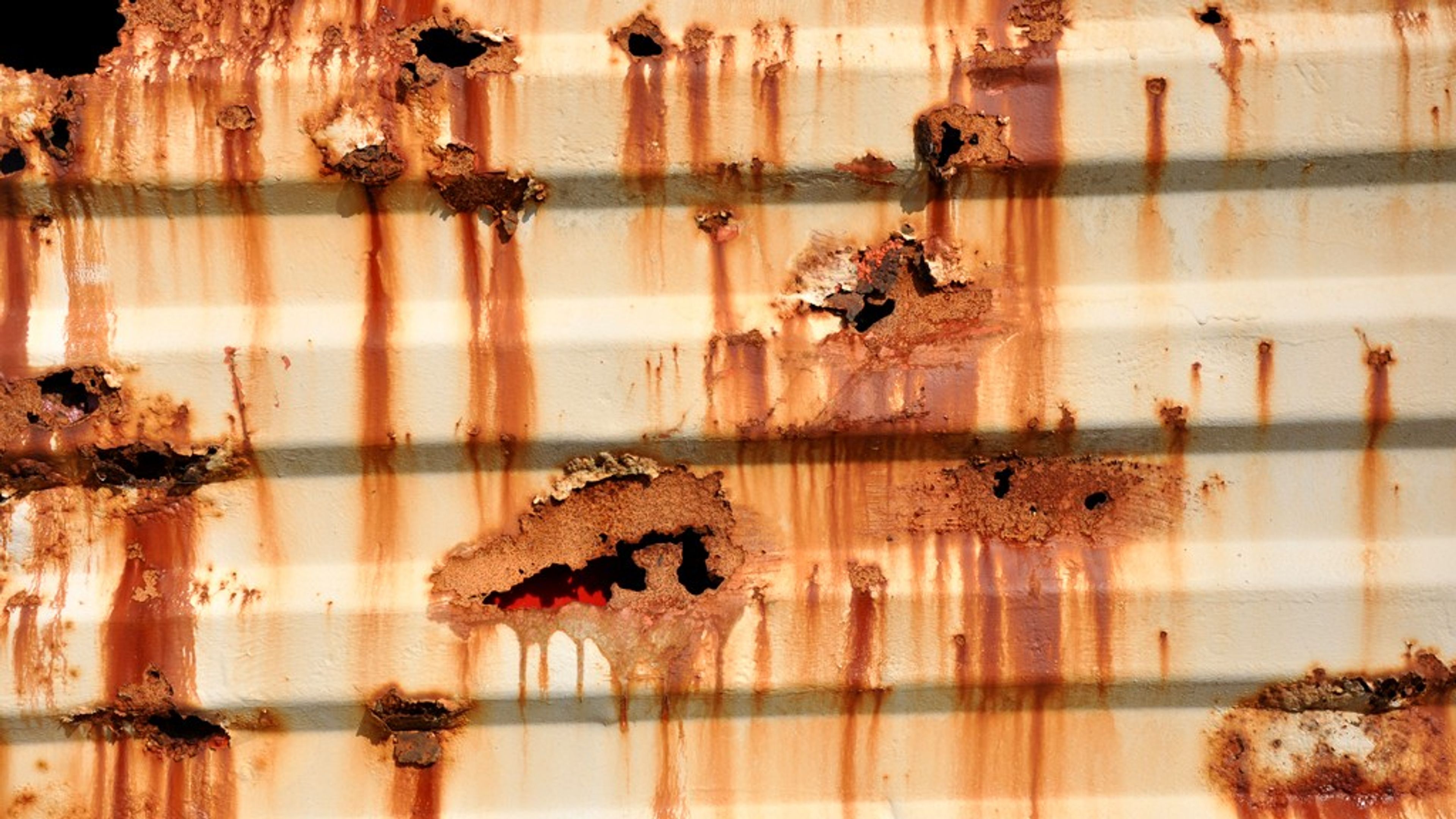 Rust bleeding through failed white paint on the corrugated wall of a shipping container