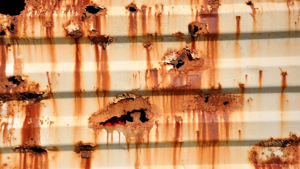 Rust bleeding through failed white paint on the corrugated wall of a shipping container