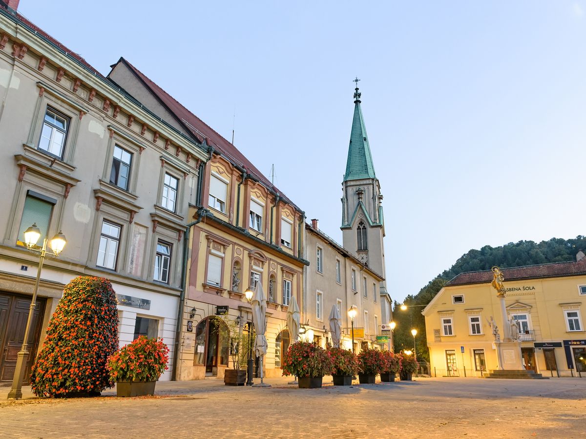 the city of Celje in Slovenia. The image features a square with historical buildings and a church spire in the background. Celje is located in the Slovenian Styria region and is known for its medieval old castle and historic town centers