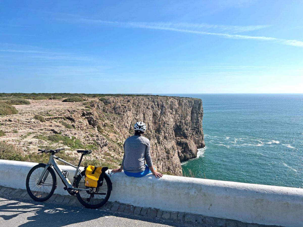 a person on a bicycle sitting on a low wall at Cape St. Vincent (Cabo de São Vicente) in Portugal, looking out over the Atlantic Ocean