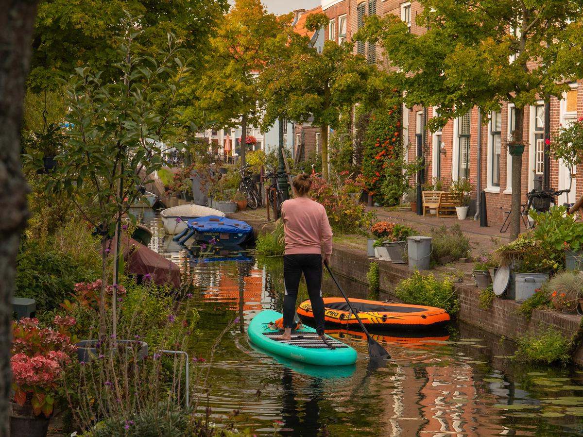 a person stand-up paddleboarding (SUP) on a canal in what appears to be the city of Leiden, Netherlands. The city is known for its canals and historic architecture