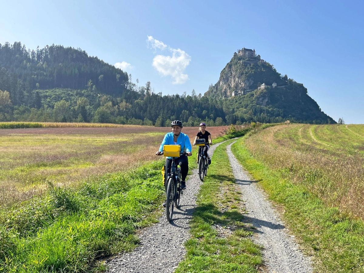 two people cycling on a dirt path with Hochosterwitz Castle in the background