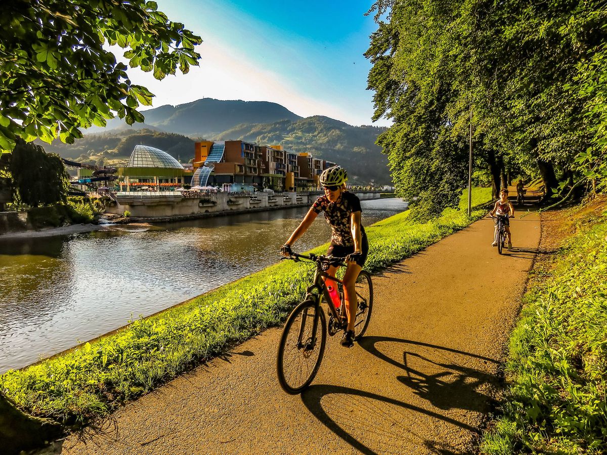 a person cycling along the Savinja River in Laško, Slovenia, with the Thermana Laško spa complex in the background