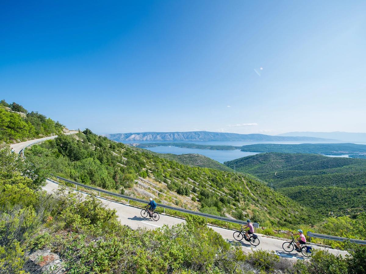 Cyclists on a winding mountain road with distant water views