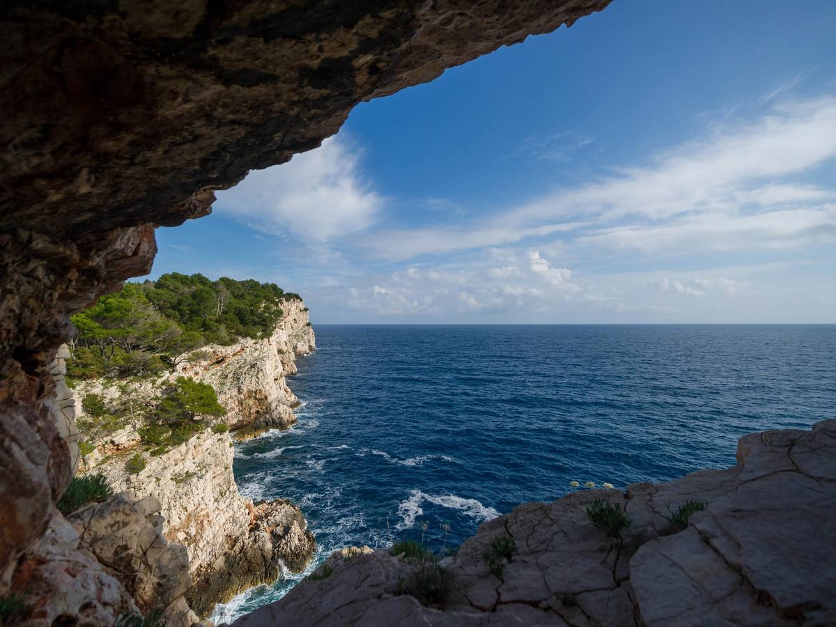 stunning coastal landscape, likely a sea cave or grotto, offering a view of the open ocean and a rugged cliffside covered in lush greenery