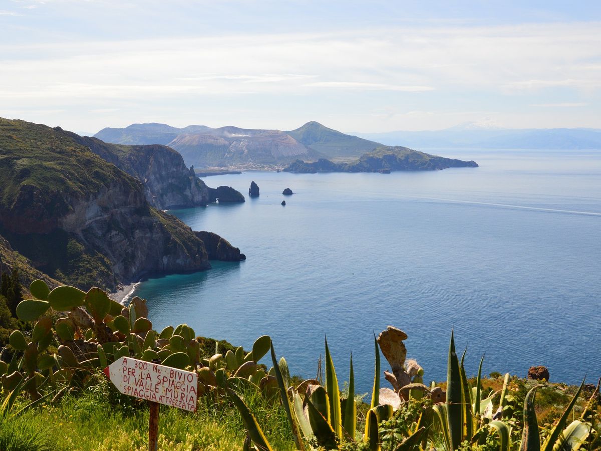 the stunning coastal landscape of the Aeolian Islands, specifically pointing towards the path to Valle Muria beach on Lipari, Italy, as indicated by the sign in the foreground