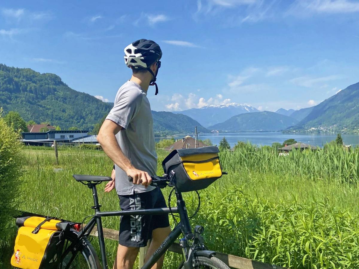 a person on a bicycle, equipped for touring with bags on the front and rear racks, pausing to admire a scenic view of a lake and mountains
