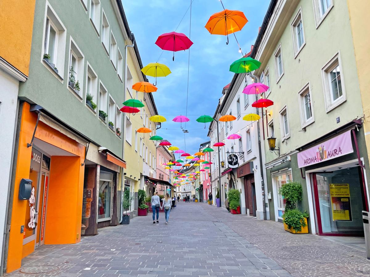 a charming street scene in Villach, Austria, specifically featuring the "Floating Umbrellas" art installation in Lederergasse