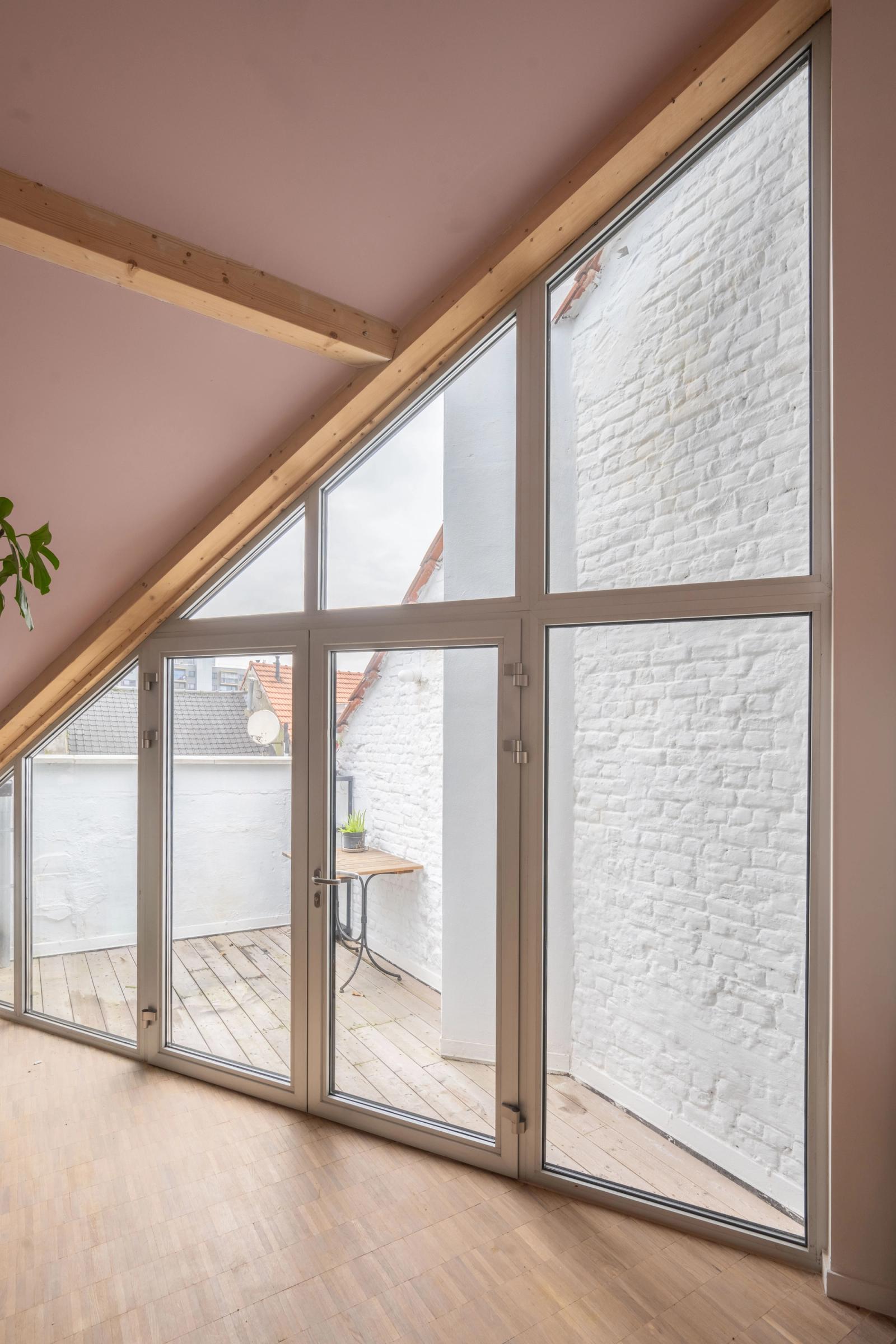 Double-height triangular window beside a red stair in a white interior