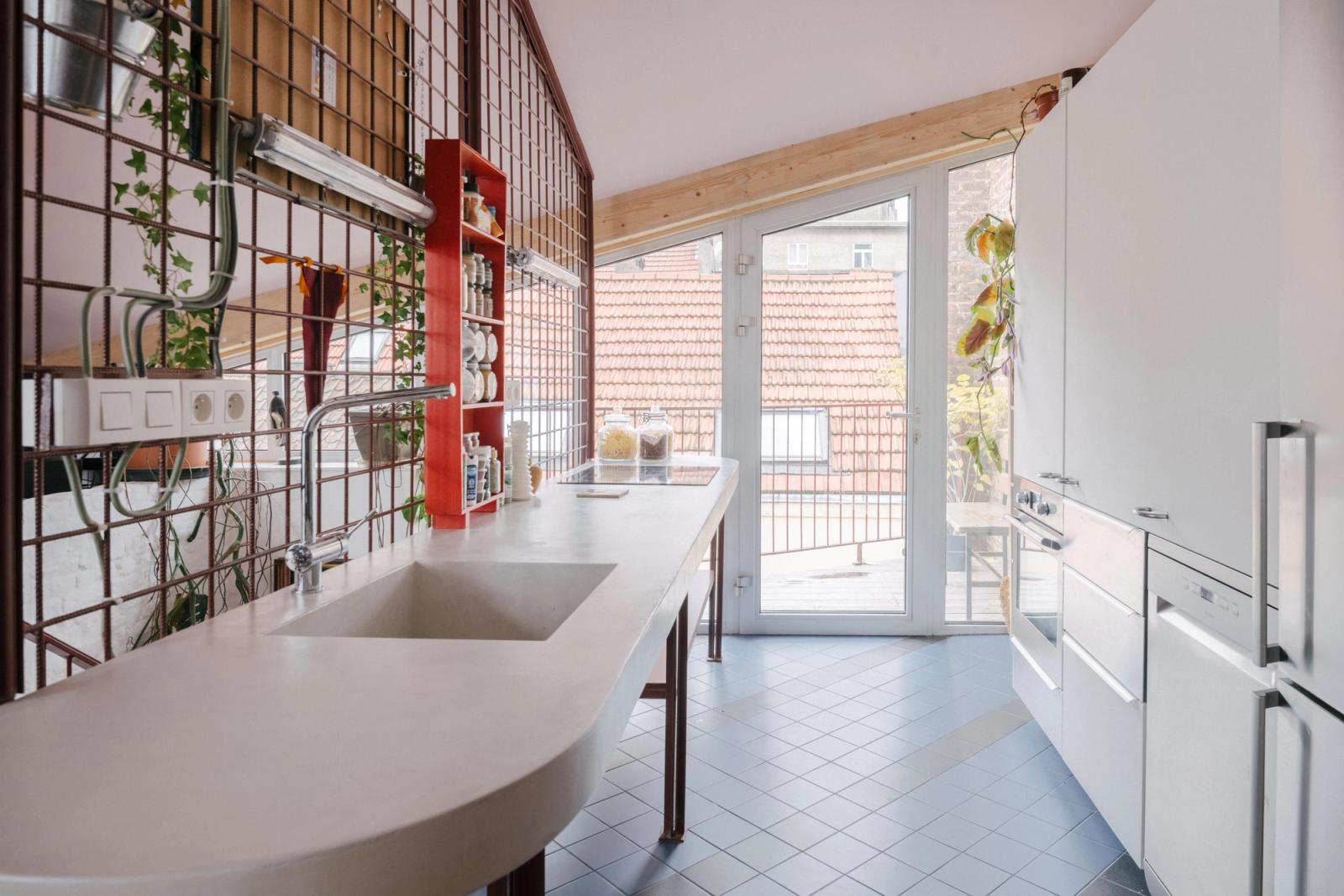Curved kitchen counter beside red mesh shelving and terrace doors