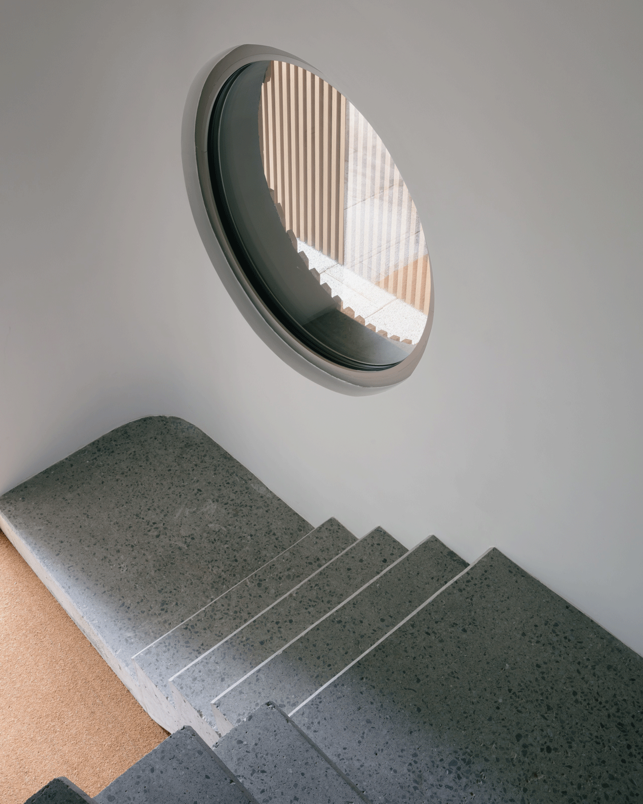Dark stair lit by a circular window in the slatted façade
