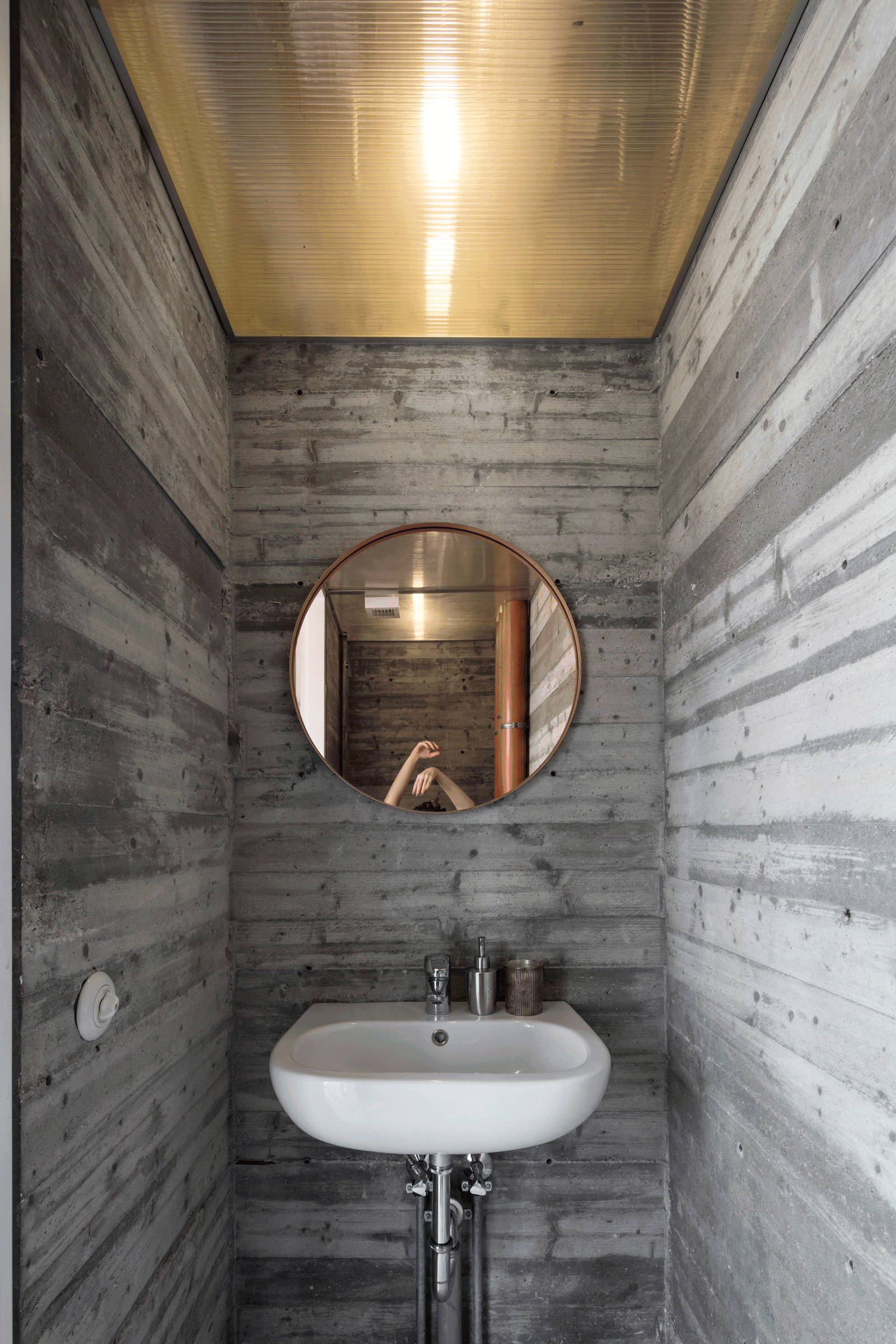 Narrow concrete washroom with a round mirror and wall basin