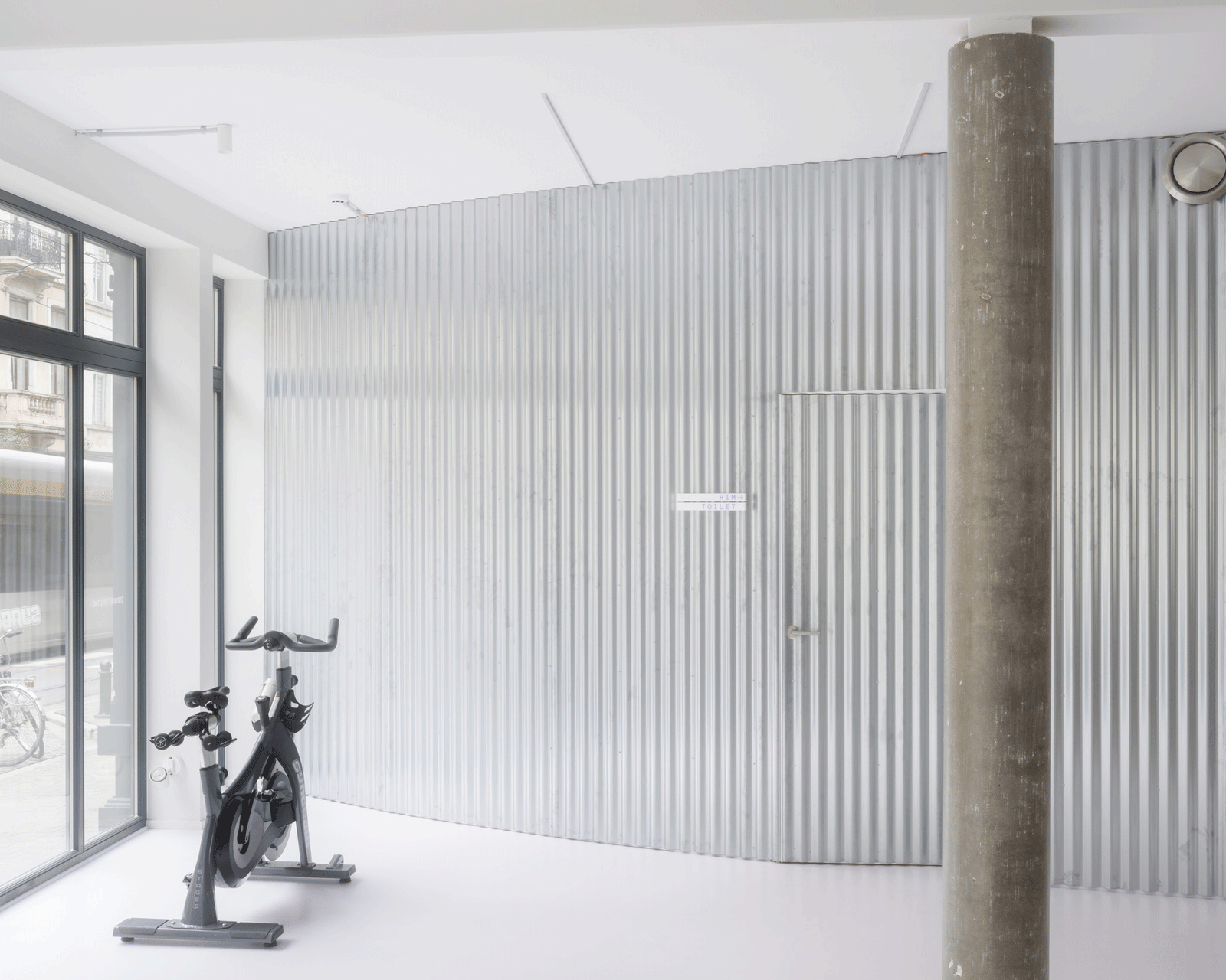 Bicycles parked beside a corrugated entrance wall and concrete column