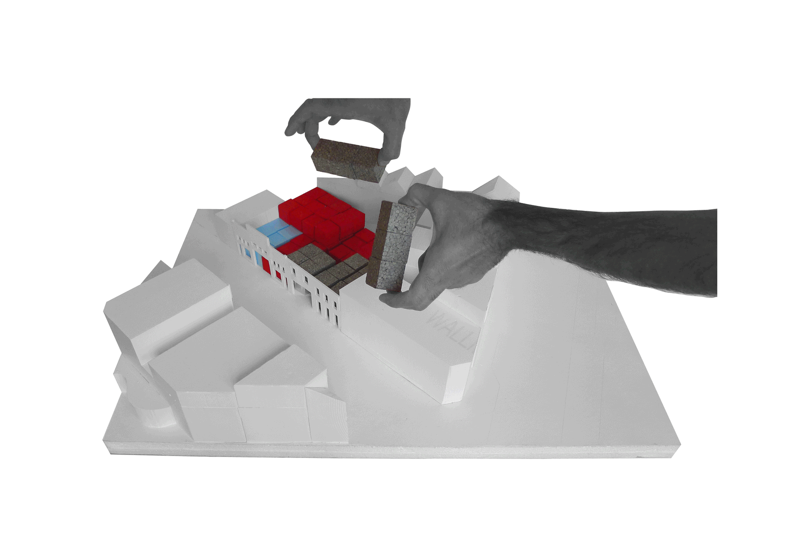 Hand placing a dark object beside red blocks in the site model