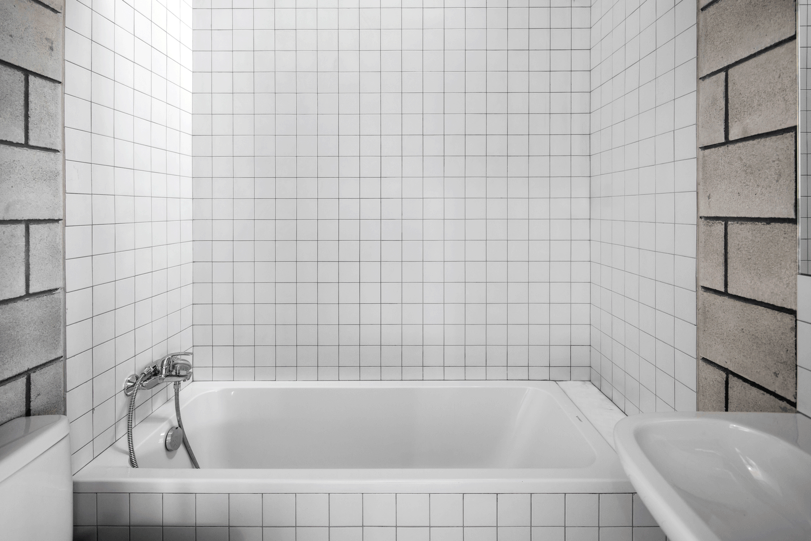 White tiled bathroom enclosed by concrete block walls