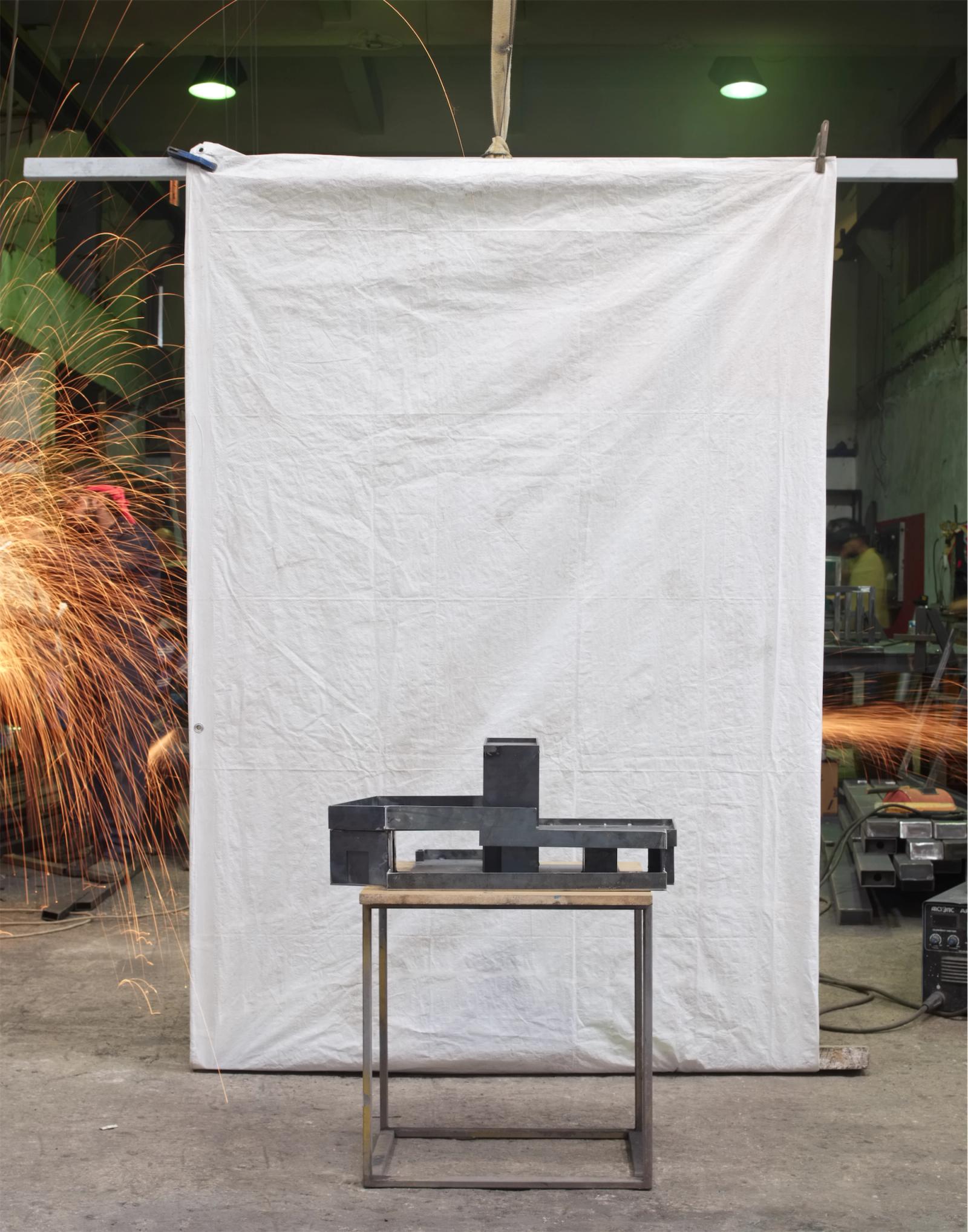 Dark exhibition object displayed before a suspended white backdrop