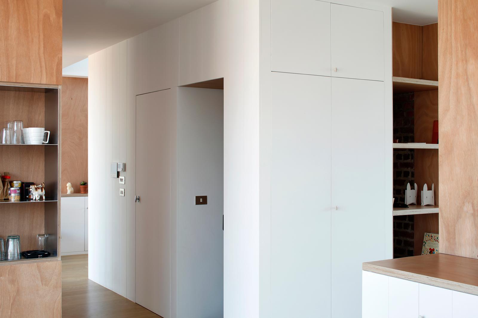 White and timber storage cabinets shaping the apartment entrance