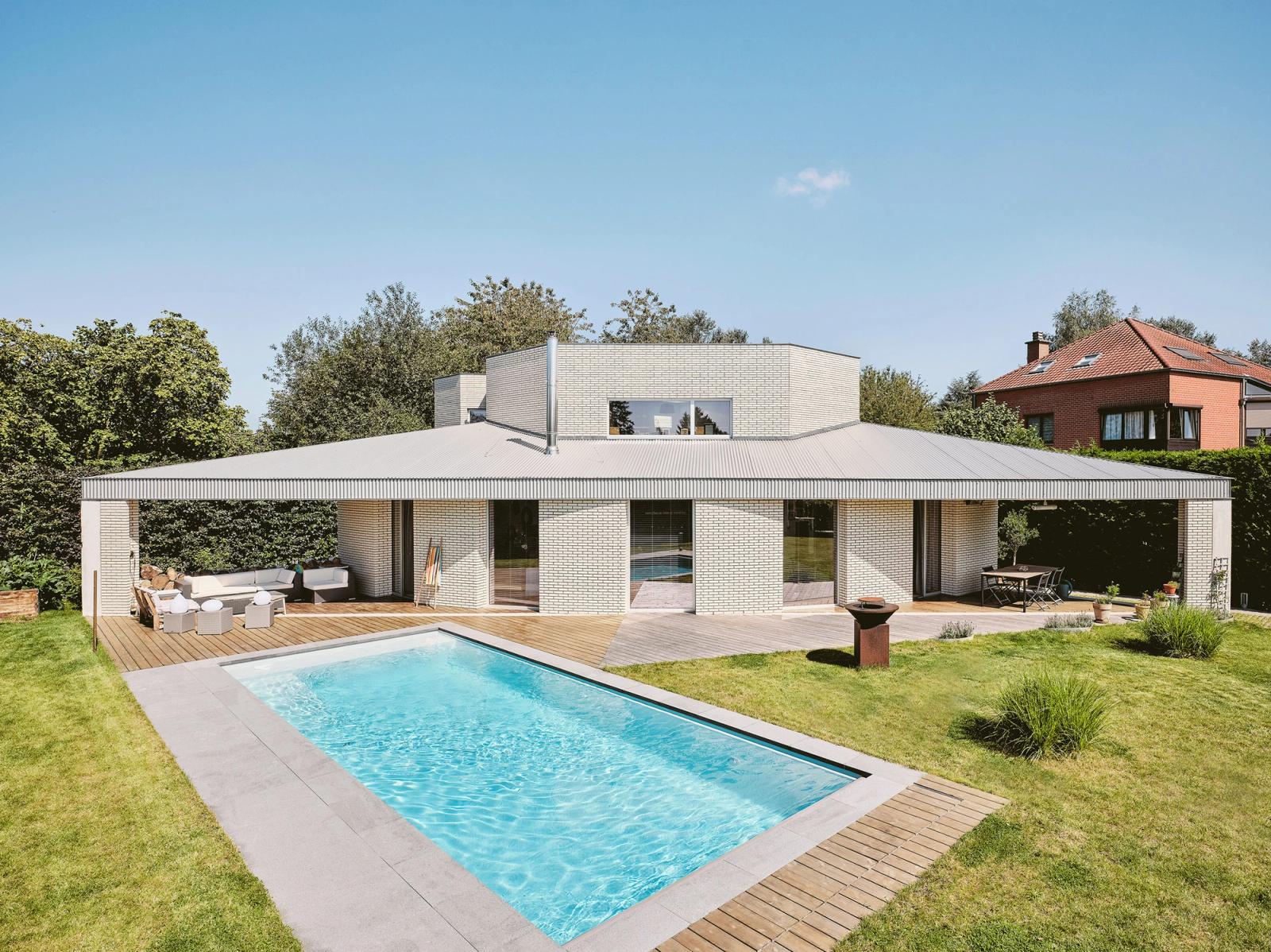 Full garden view of the low brick house beside a swimming pool