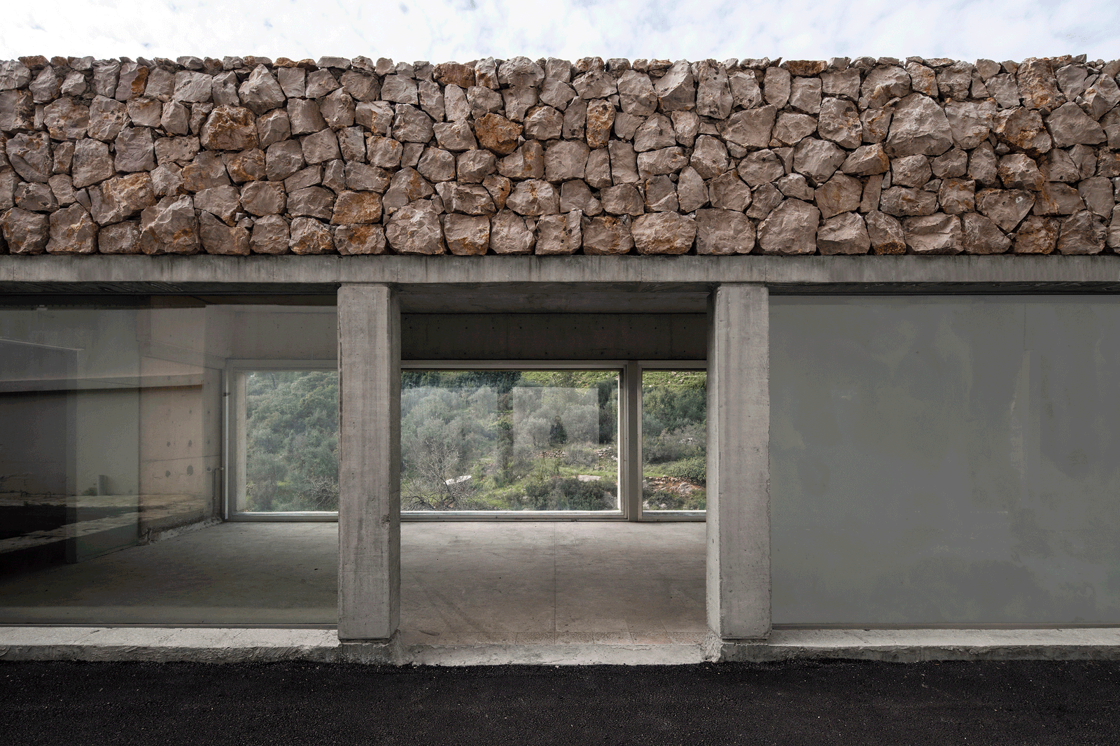 Concrete façade opening beneath a thick dry-stone parapet