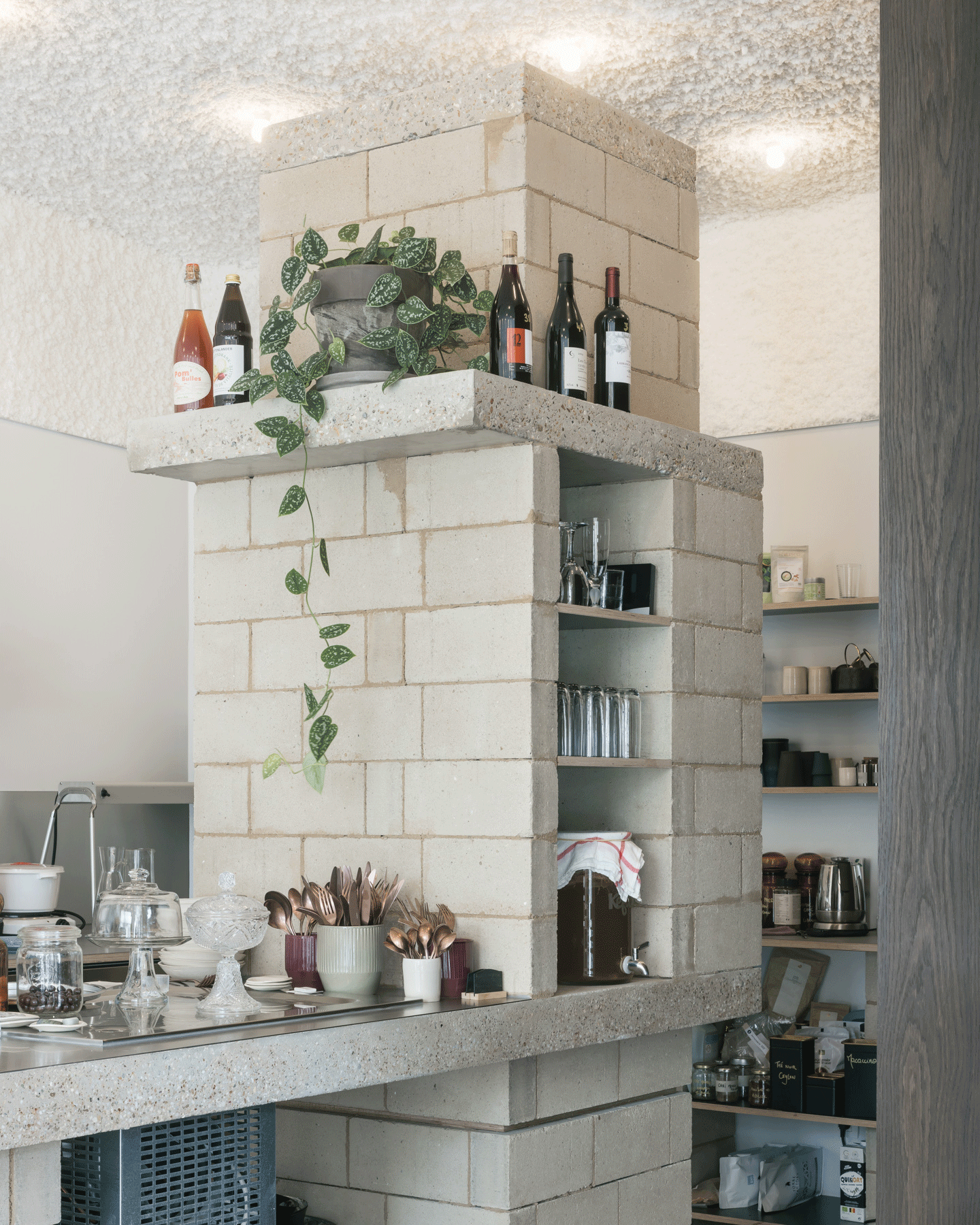 Terrazzo-block island supporting plants, bottles and open shelving