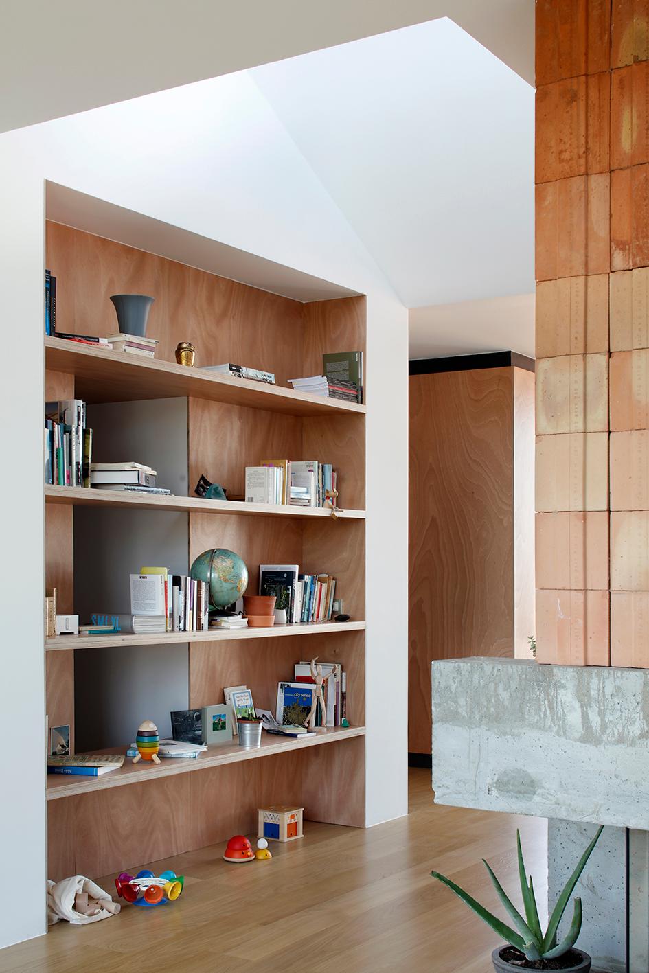 Timber bookshelves meeting the tiled fireplace at the living-room corner