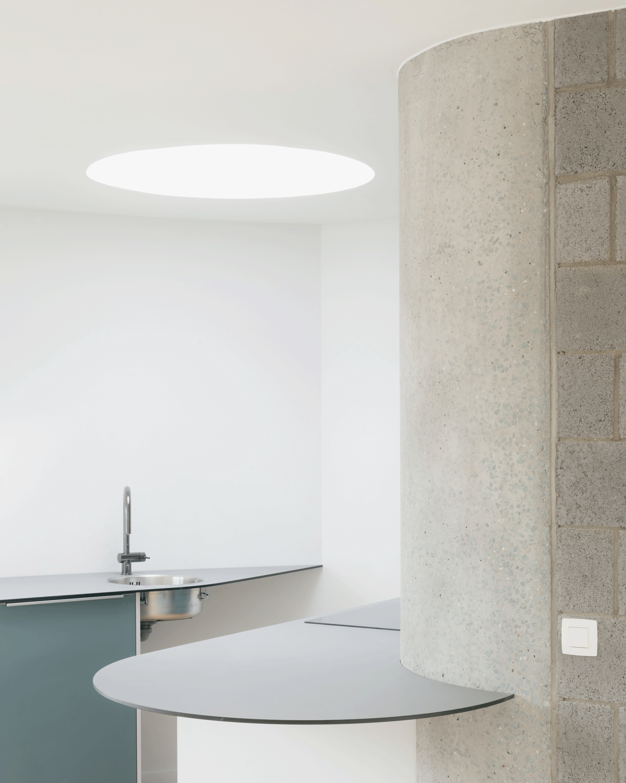 Curved kitchen island beside a concrete core and round skylight