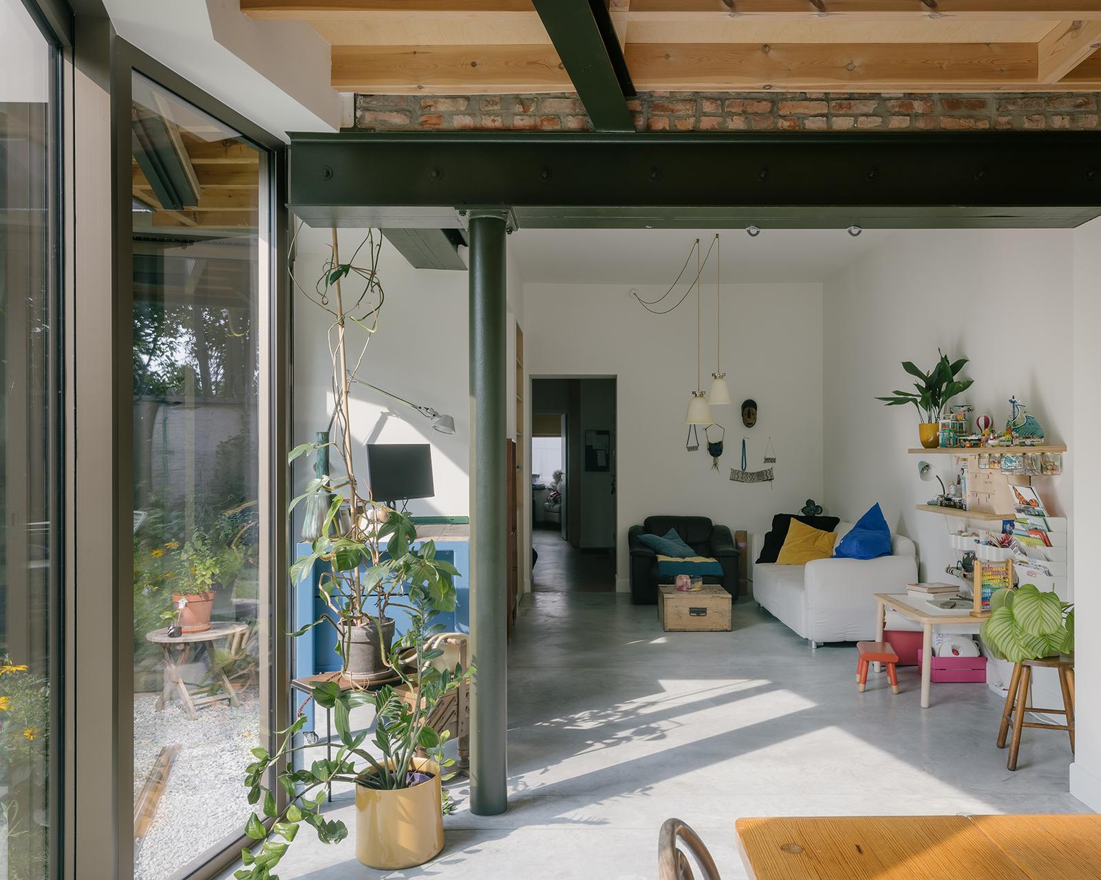 Sunlit living extension framed by a dark green steel beam