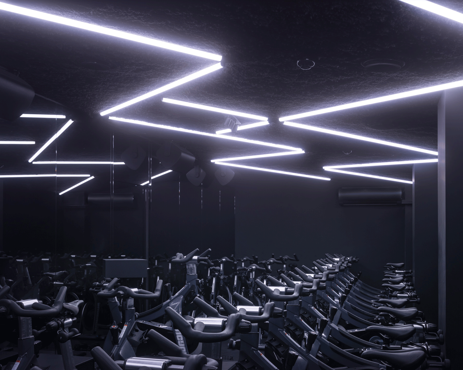 Dark cycling studio lit by zigzagging white ceiling strips