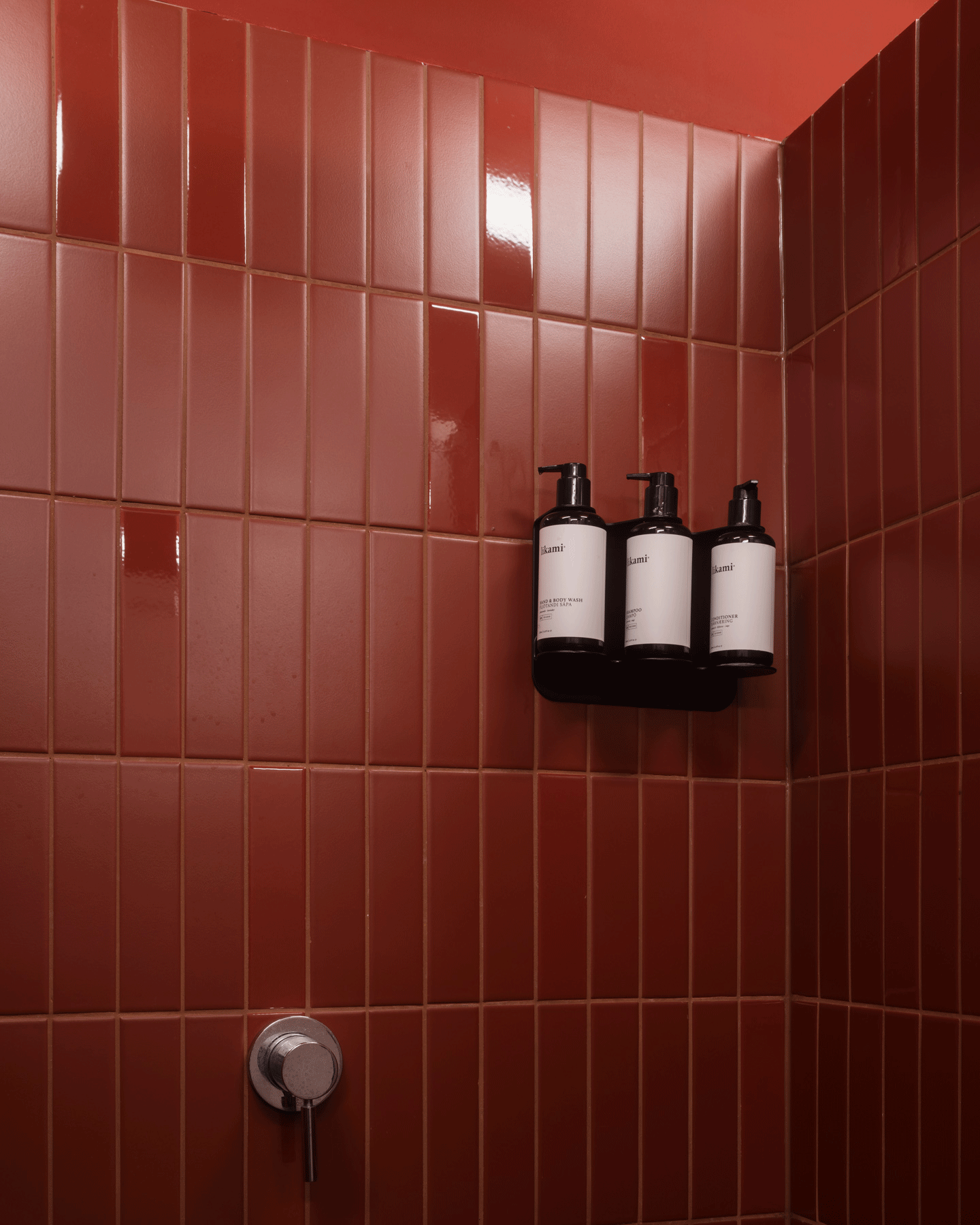 Red-tiled shower wall with black dispensers and metal controls