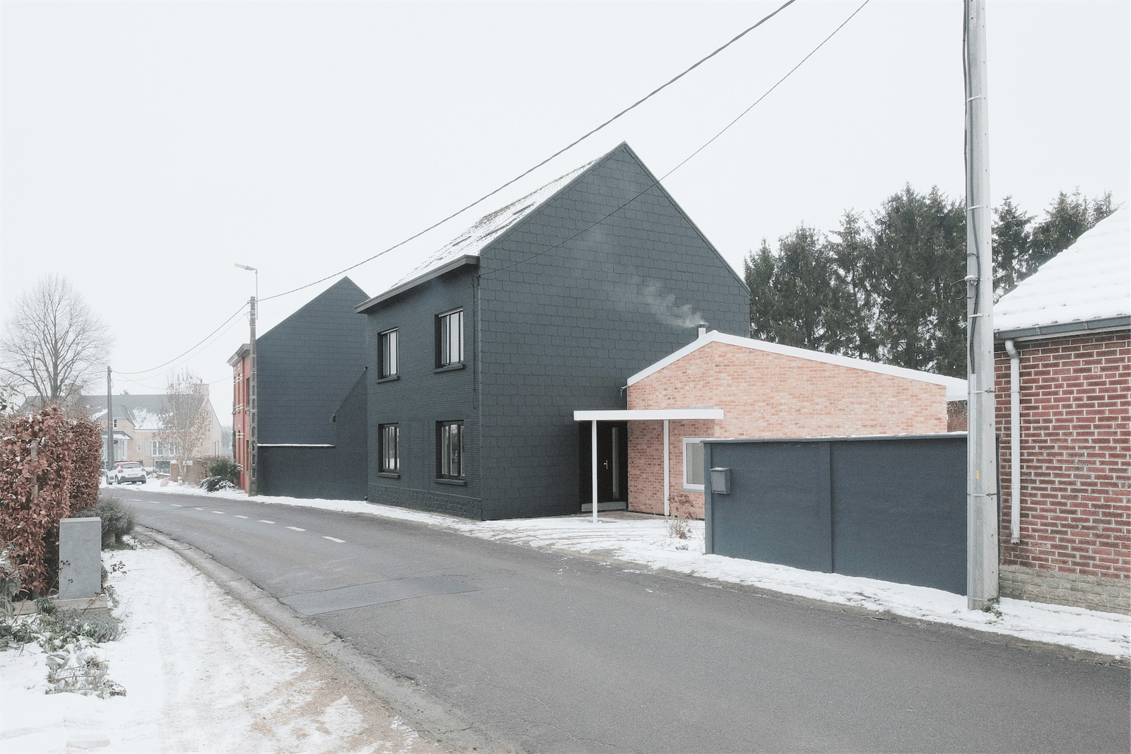 Snowy street view of the dark house and attached garage