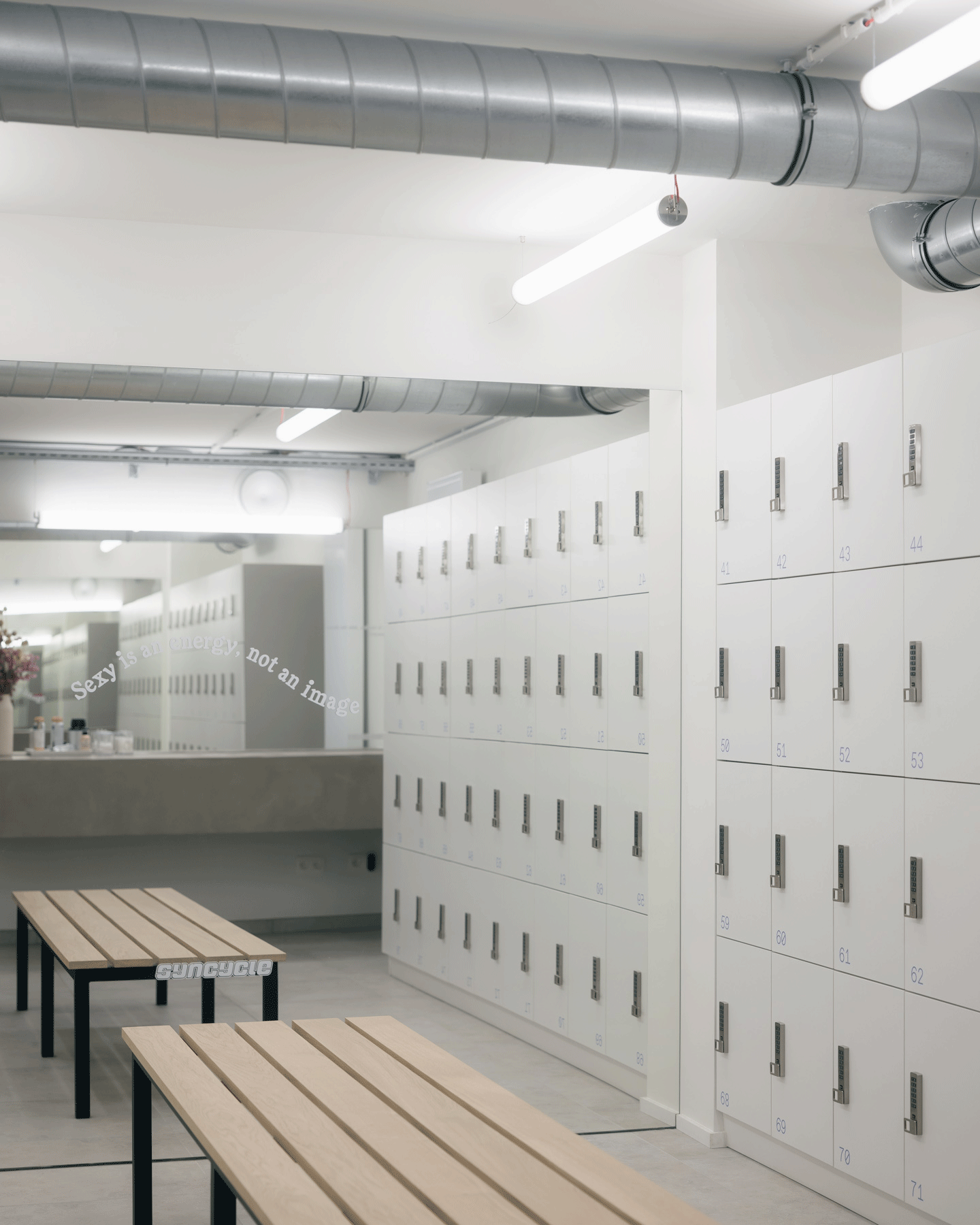 Locker room with pale benches, metal ducts and a long cabinet wall
