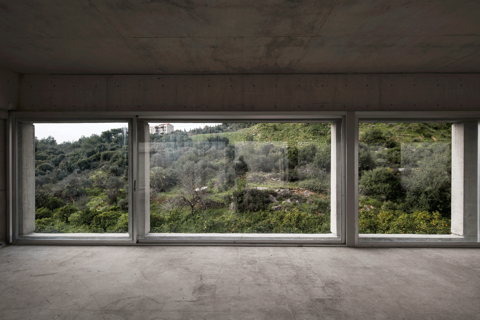 Concrete room with a long window framing the green hillside