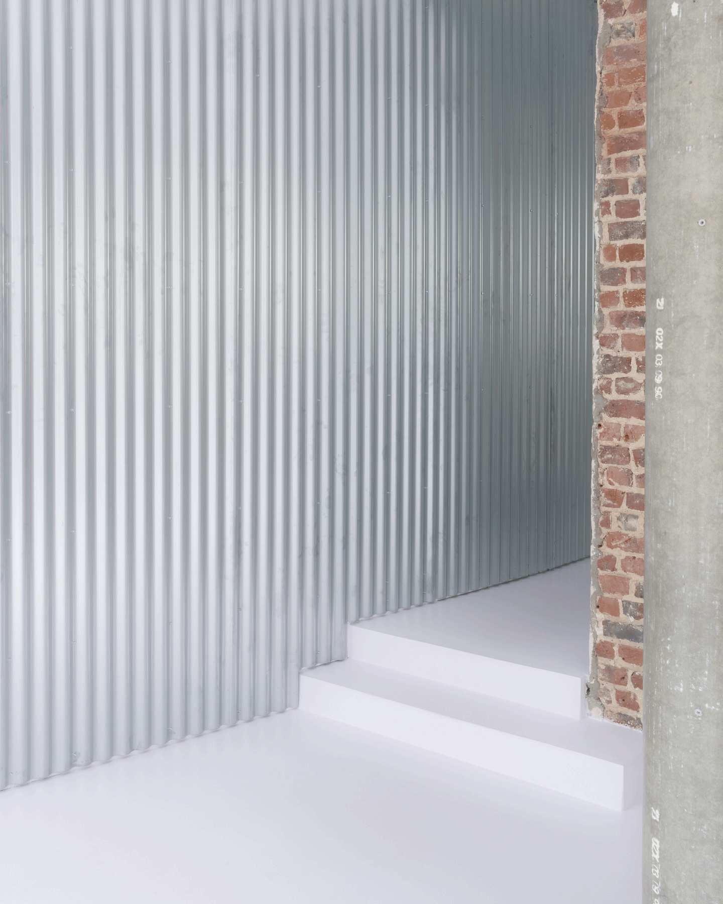 White stair rising beside a corrugated wall and retained brick pier