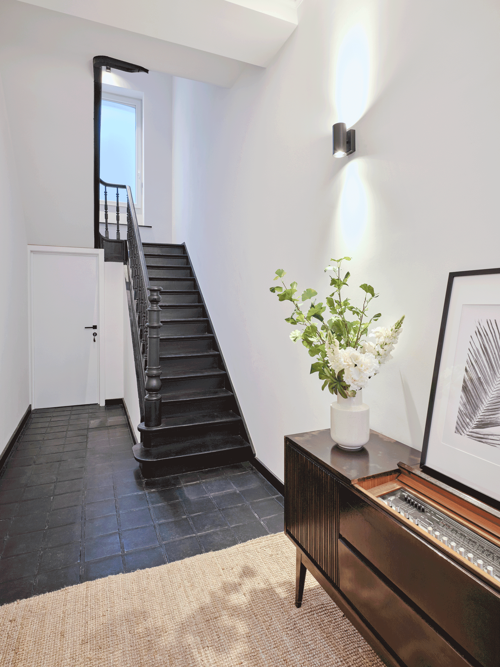 Dark stair rising through a white entrance hall