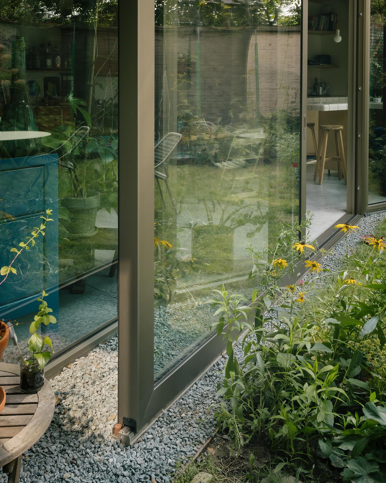 Glazed façade reflecting dense planting at the garden edge