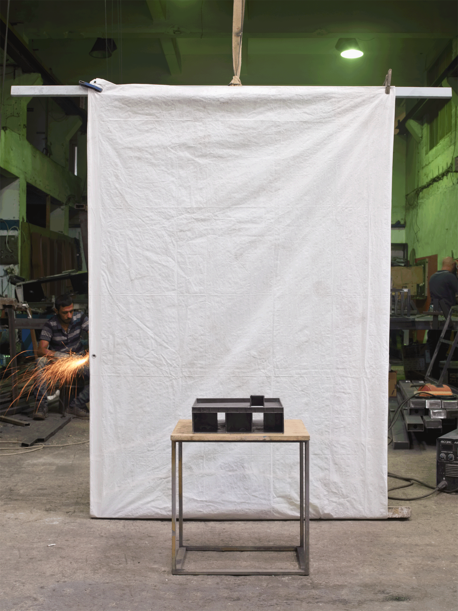 Small dark object displayed on a stool before a white fabric backdrop