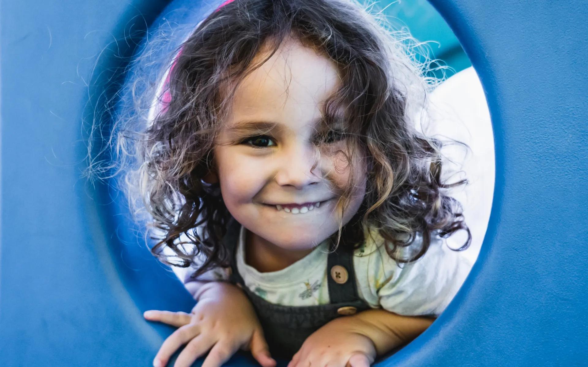 A photo of a little girl looking through a playground slide.