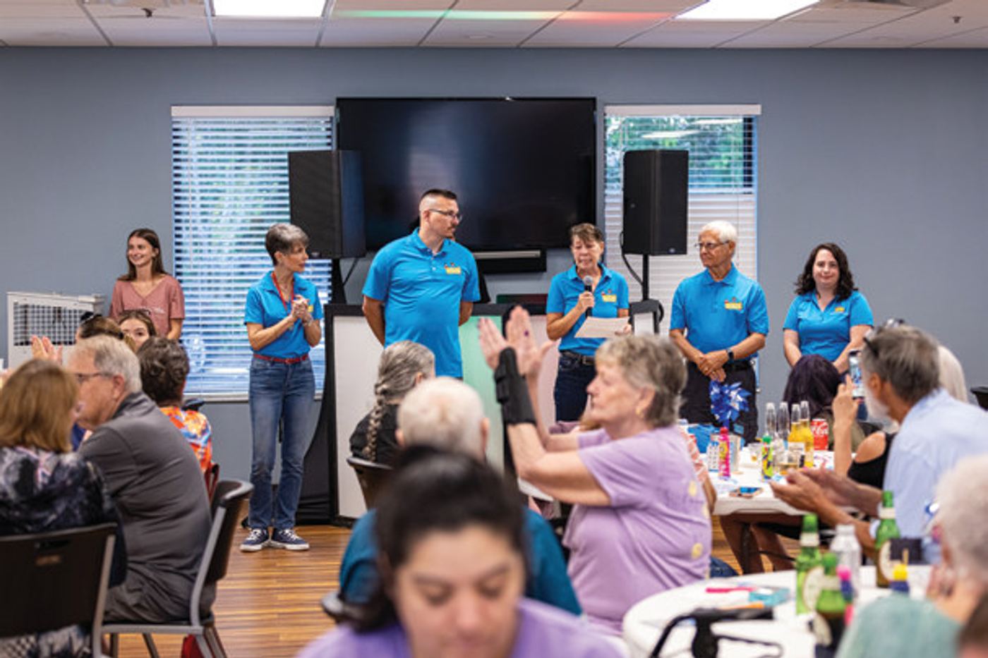 < Board members of Seminole County Friends of Abused Children address the organization’s supporters at a fundraising event.