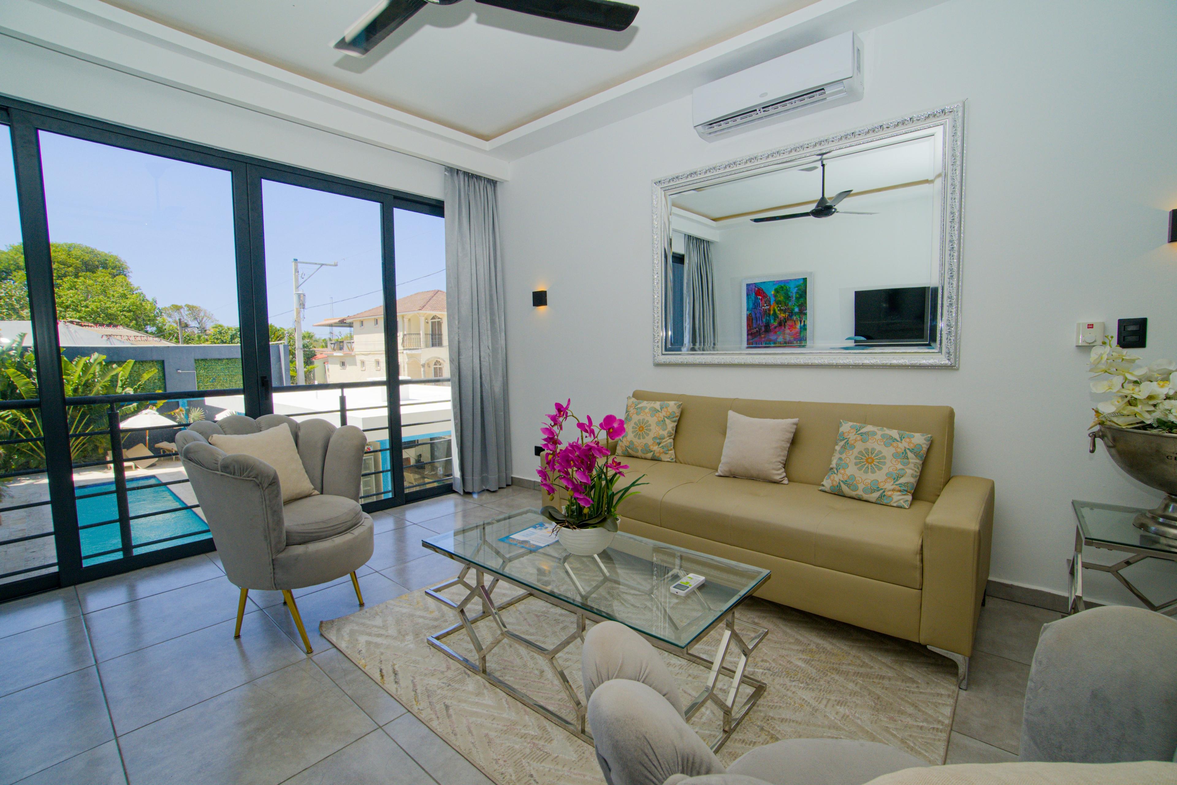 Living room with a cream sofa, glass coffee table and doors to the pool