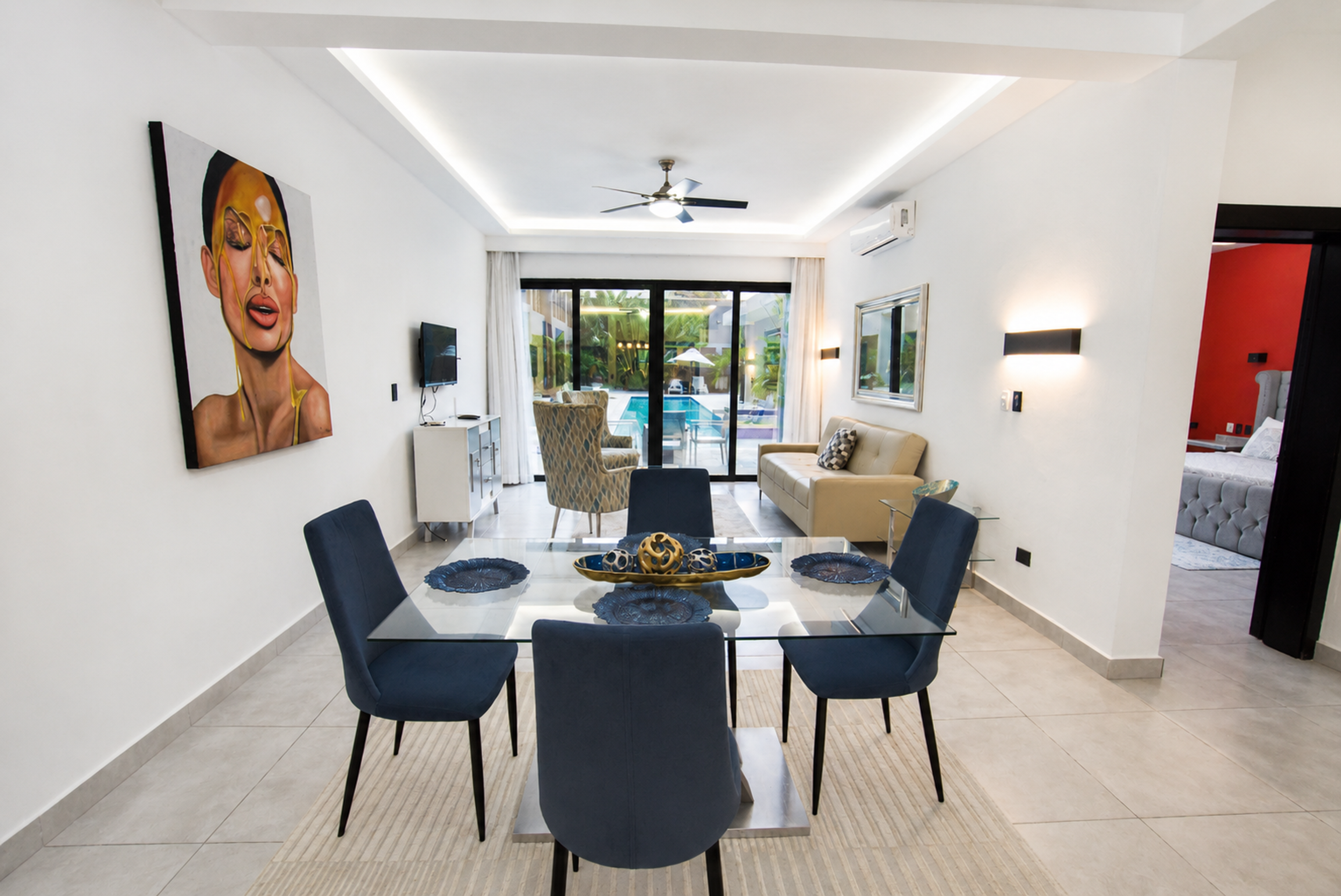 Dining table set for six with blue velvet chairs, beside a portrait mural and the balcony doors