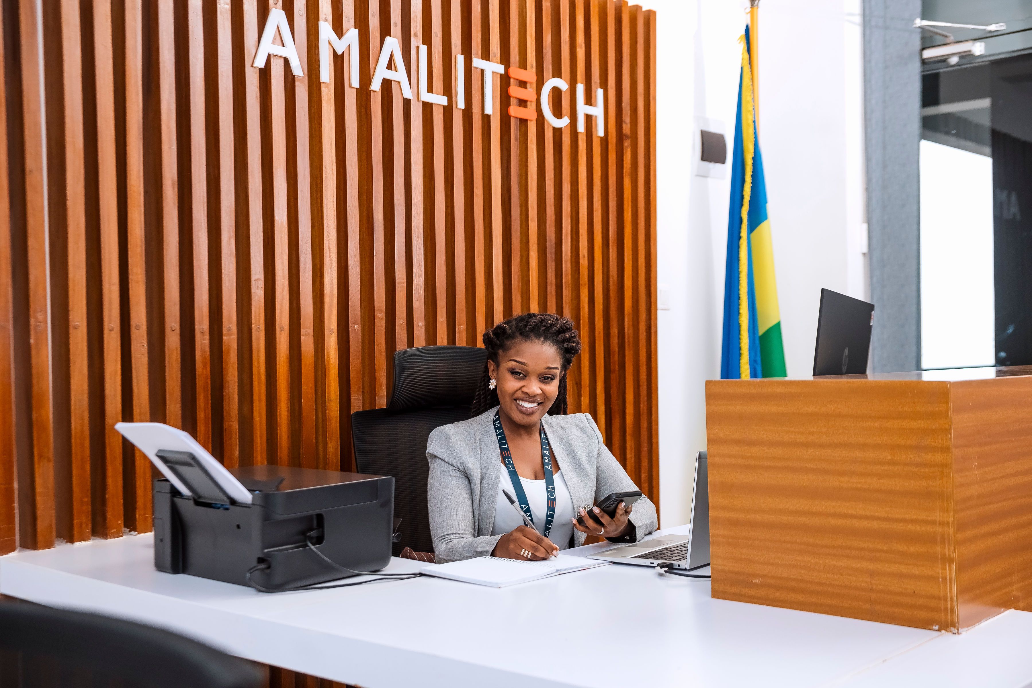  A lady seated at the reception of our Kigali office, smiling, with a Rwanda flag at the background