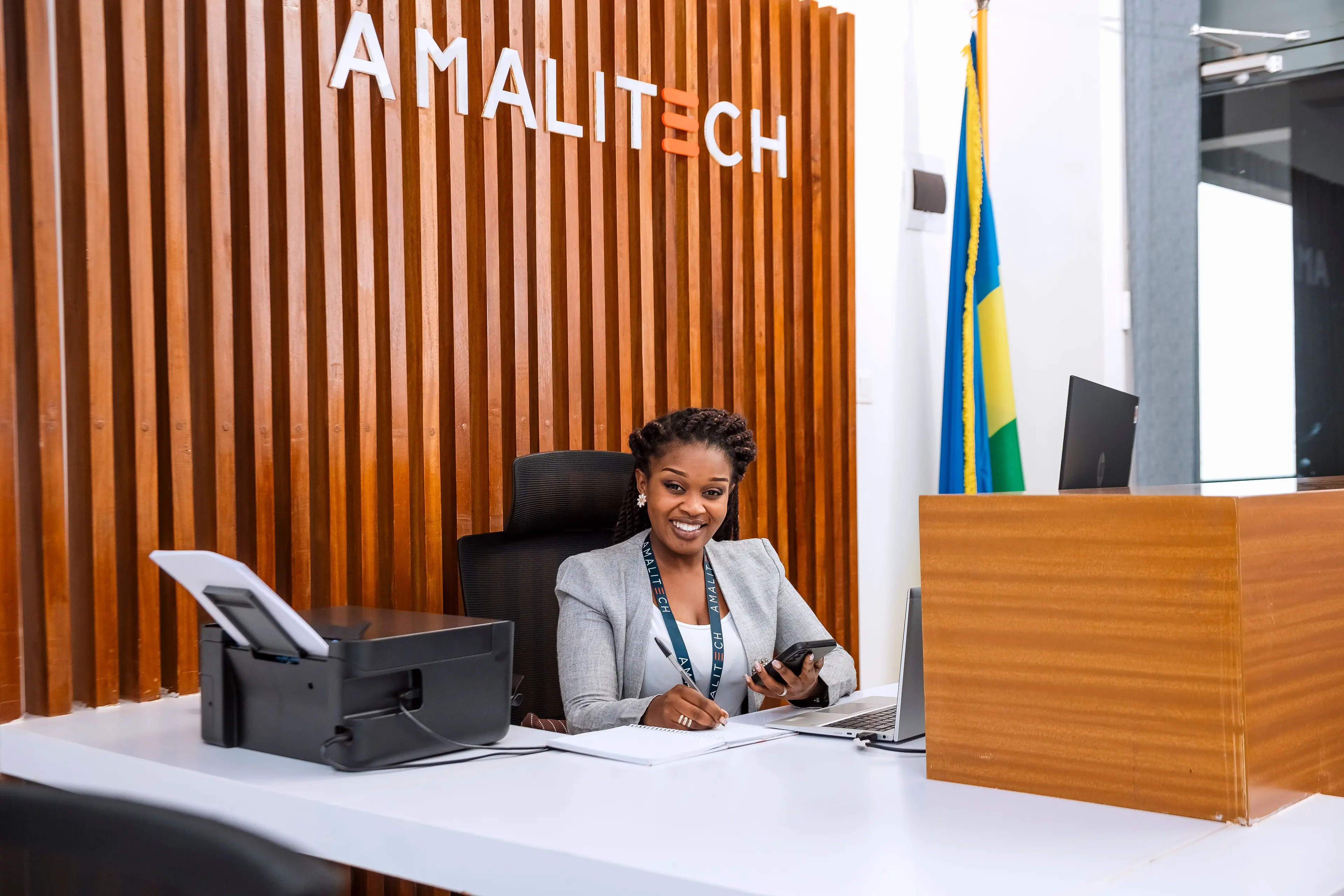 A lady seated at the reception of our Kigali office, smiling, with a Rwanda flag at the background