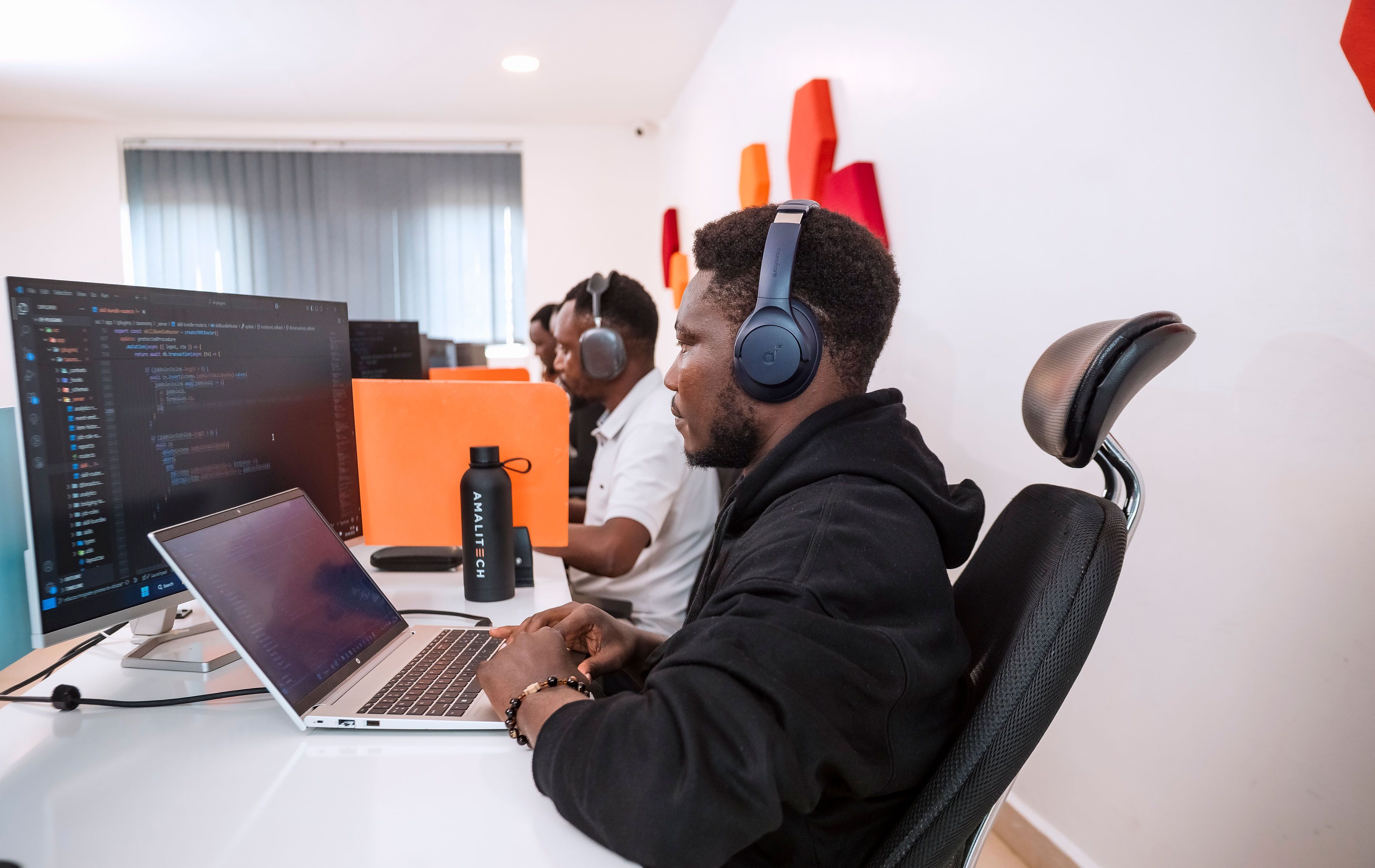 a man wearing headphone, working at his desk, using his laptop and additional big screen